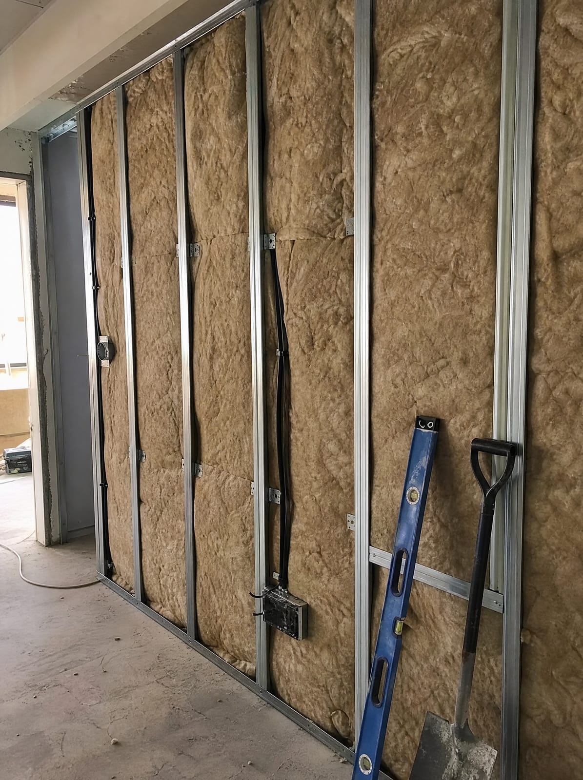 Open partition wall cavity showing insulation batts fitted between metal studs before boarding