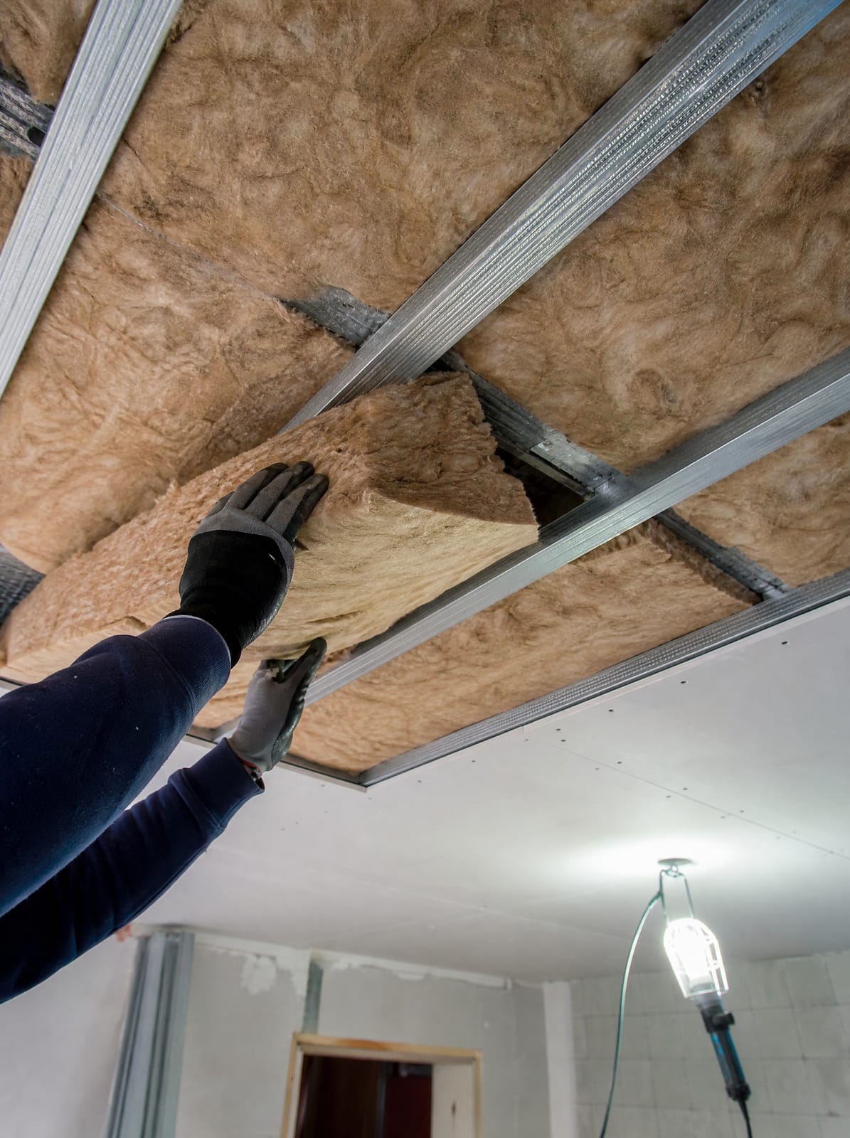 Insulation batts being installed above a partially finished plaster ceiling frame