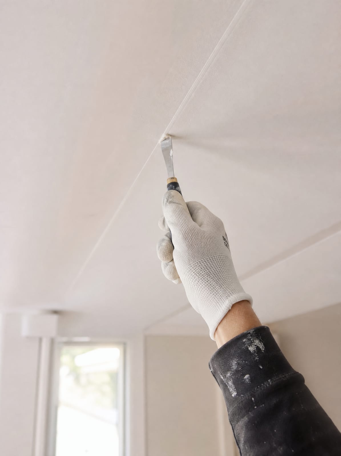 Contractor's gloved hand doing a close inspection touch-up on a finished plaster ceiling joint