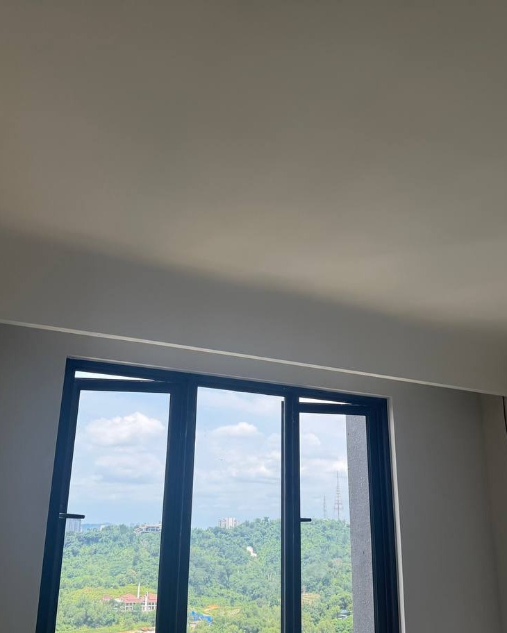 Curved plaster ceiling with concealed cove lighting above black-framed window overlooking green hillside, Bangsar residential ceiling design