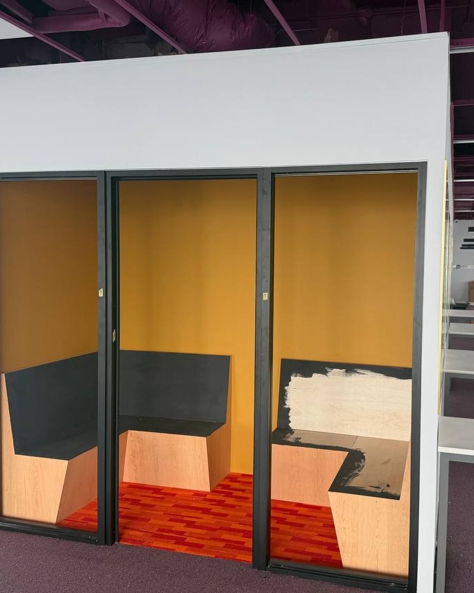 Three soundproof partition booths with plaster ceiling bulkhead in Brickfields office, mustard yellow walls and black-framed openings above built-in wooden bench seating