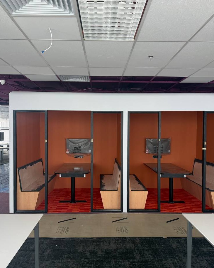 Suspended grid ceiling above glass-partitioned meeting booths featuring orange feature walls and built-in banquette seating, Brickfields office fit-out