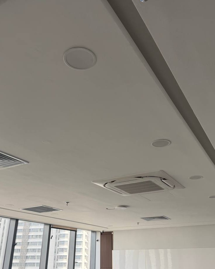 White plaster ceiling in Brickfields office with recessed downlight trims, ceiling speakers, and built-in cassette air conditioning unit alongside a stepped bulkhead detail