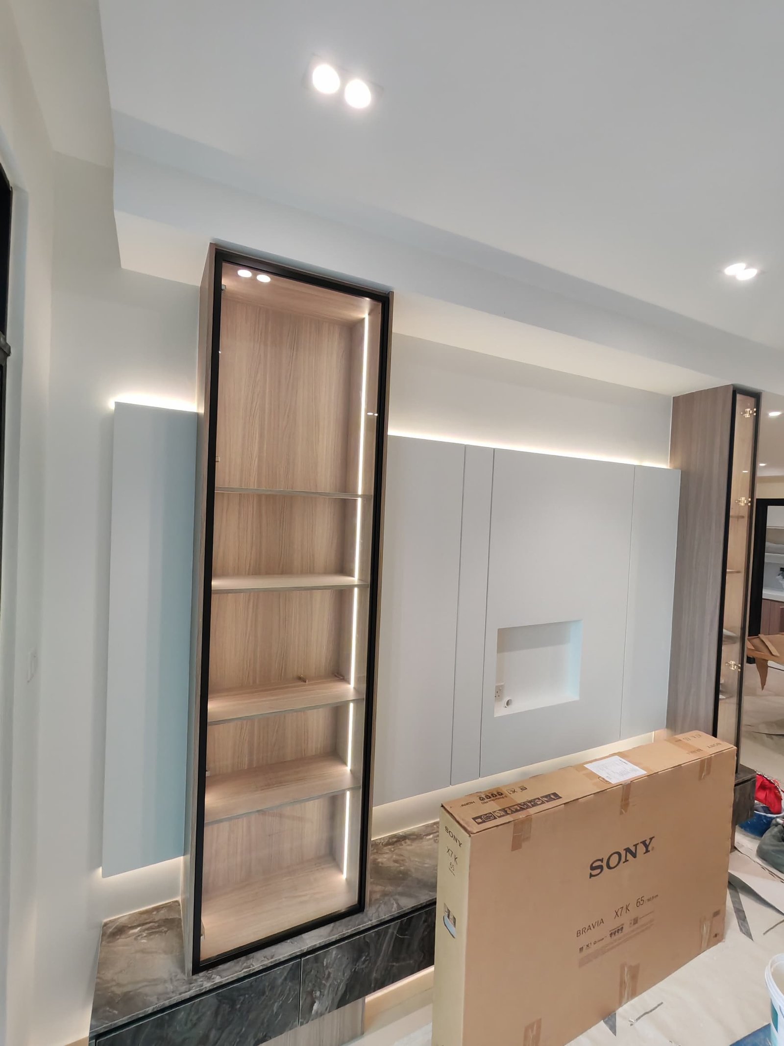 TV Wall and Backlit Display Shelving – Sungai Long TV feature wall beside a backlit open shelving display cabinet with LED-lit shelves, television still boxed on the floor, Sungai Long home renovation