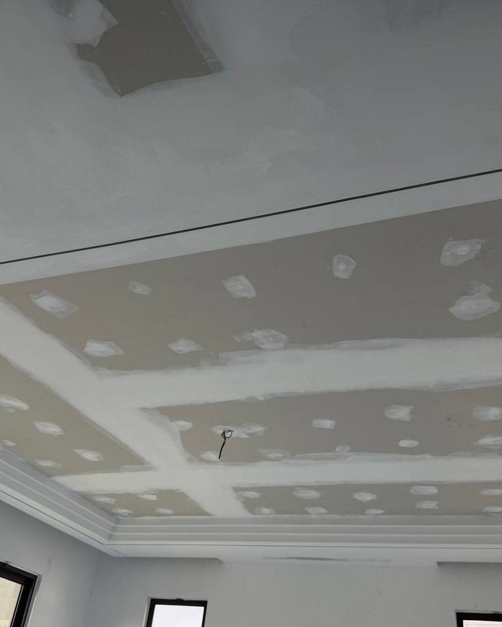 Unfinished plaster ceiling with joint compound patches and taped seams, recessed drop panel and cove lighting ledge under construction, Cyberjaya residential staircase project
