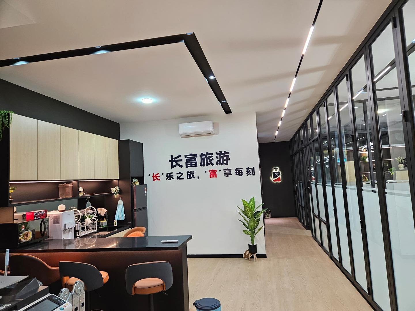 Angled LED Ceiling Strip Above Pantry Corridor - Kepong Angled linear LED ceiling strip above a pantry counter and glass partition wall corridor, Longrich Tour & Travel signage on wall, Kepong office fit-out