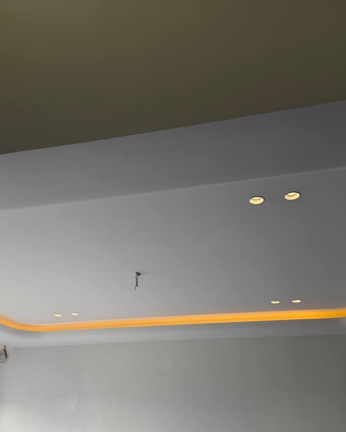 Multi-level drop plaster ceiling in Klang residence with recessed downlights and curved cove lighting channel emitting warm amber glow