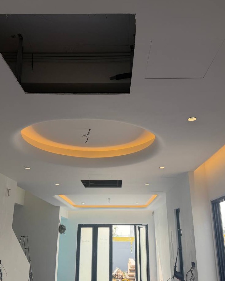 Round plaster ceiling cove with hidden LED light trough and recessed downlights in Klang residence hallway, showing unfinished access panel cut for electrical wiring overhead