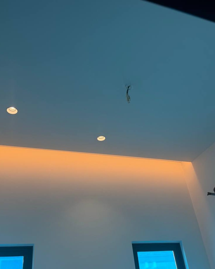 Flat plaster ceiling with recessed downlights and hidden cove lighting casting warm orange glow along curtain box edge, Klang residence upper floor