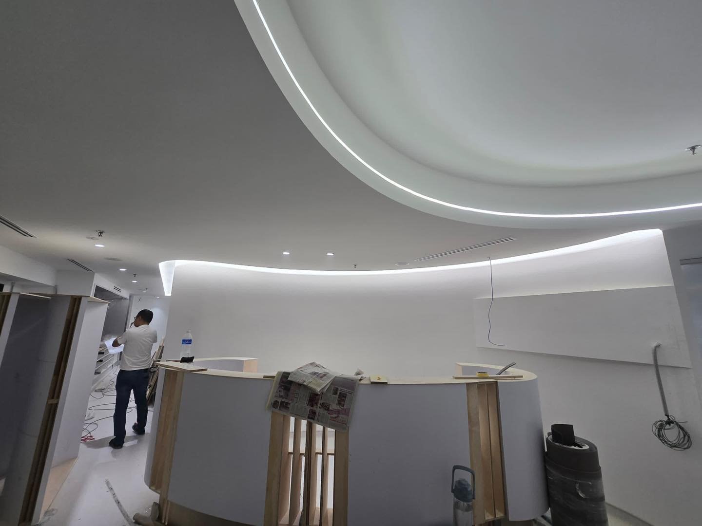 Curved Ceiling with Continuous LED Profile – Mid Valley Flowing S-curve plaster ceiling bulkhead with continuous LED profile strip above a curved reception counter under construction, Mid Valley salon fit-out