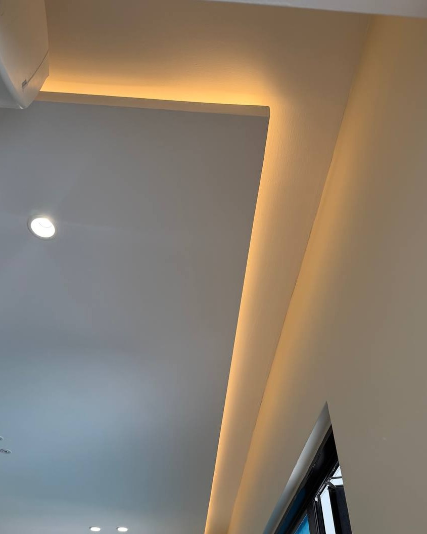 Plaster ceiling drop with concealed cove lighting along ceiling-to-wall corner in Rawang residential ground floor home, warm LED strip highlighting curved plaster edge beside recessed downlight