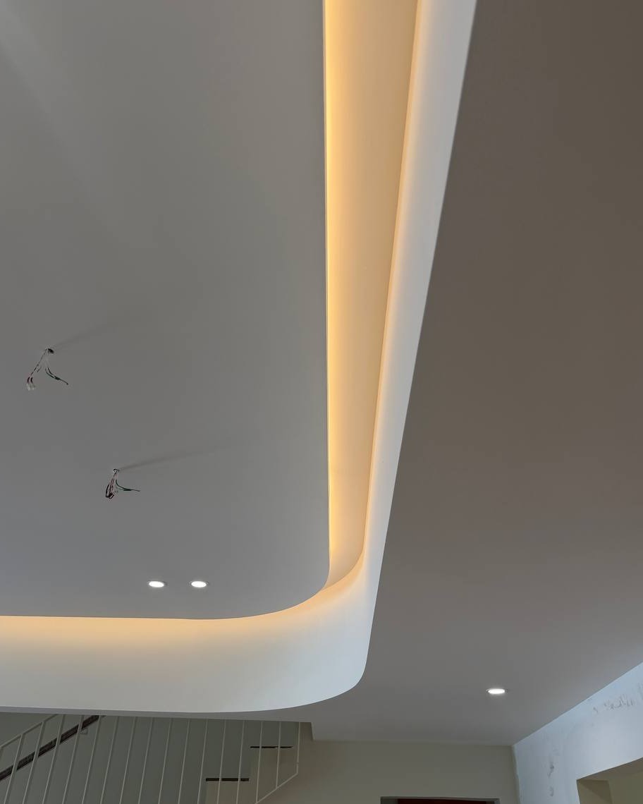Curved plaster ceiling with hidden cove lighting channel above a staircase in a Rawang residential ground floor, showing recessed LED downlights and pending pendant light wiring