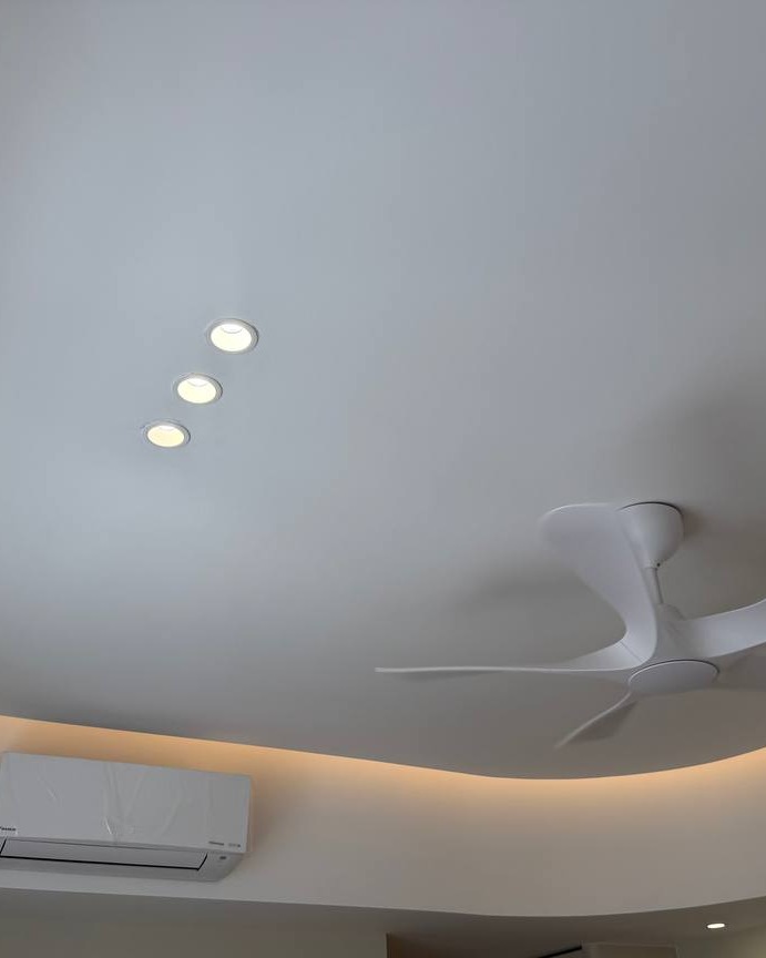 Curved plaster ceiling in Rawang home with recessed LED downlights, modern white ceiling fan, and warm LED strip lighting concealed along the curved drop edge above an air conditioning unit