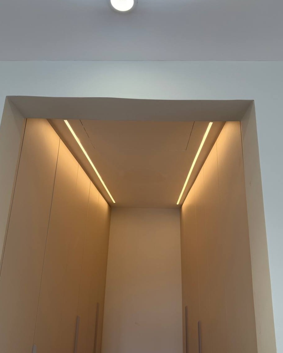 View looking up into a wardrobe alcove in Rawang with plaster ceiling recess and two parallel warm-toned LED strip lights running along the sloped ceiling edges above built-in cabinet doors