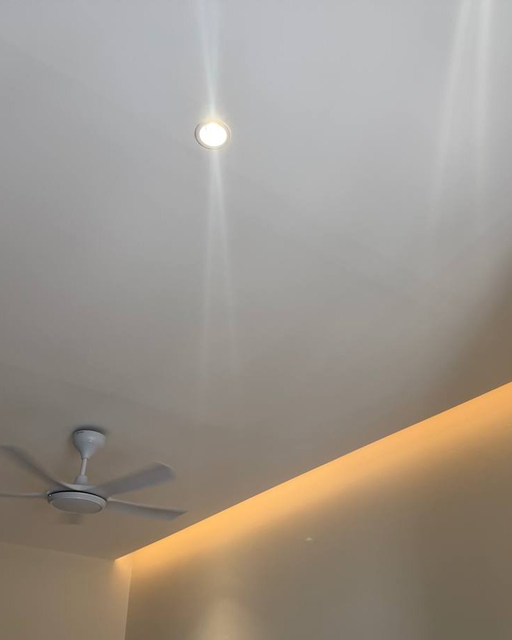 Flat plaster ceiling in Rawang home with recessed spotlight and warm LED strip lighting tracing a curved cove edge, ceiling fan mounted nearby