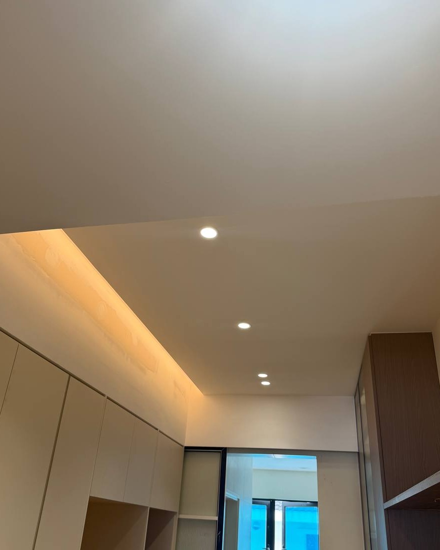 Flat plaster ceiling with recessed downlights and warm cove lighting above white cabinetry in a Rawang residential hallway