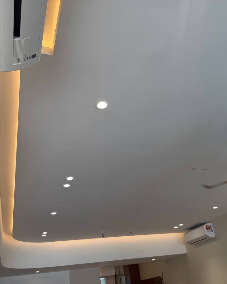 Curved plaster ceiling with cove lighting and recessed LED downlights in Rawang residential ground floor, showing indirect warm light strip along the drop-down border and split unit air conditioner fitted into the design