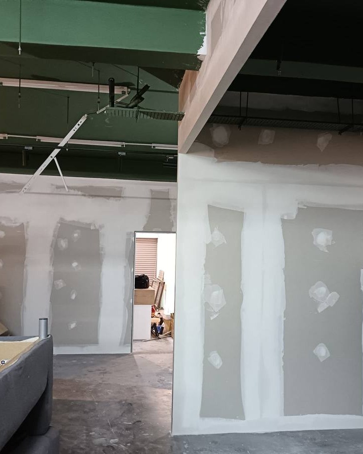 Plaster Partition Wall Installation – Shah Alam Office Skim-coated plasterboard partition walls with jointed seams and screw-patched sections in Shah Alam office fit-out, exposed green ceiling beams and concrete floor visible during construction